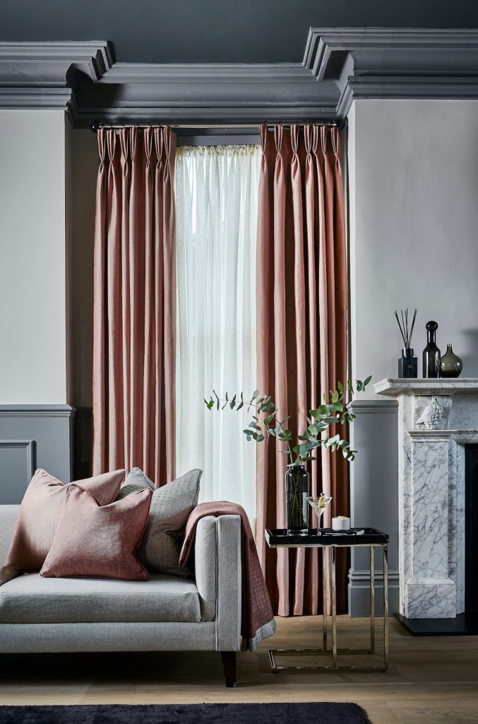 A traditional room with high ceilings and large windows framed by long silk curtains in a coppery colour.